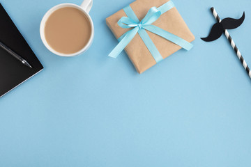 Fathers day. Gift box, cup with coffee, note pad and black paper mustache on light blue table. Top view, flat lay, copy space