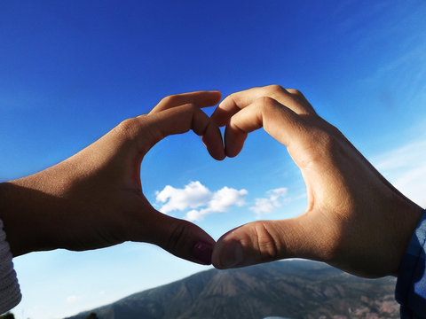 Close-up Of Hands Making Heart Shape Against Blue Sky