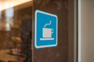 Close up to sticker of symbol coffee shop on glass background. Cafe wallpaper view. sticker on the window with a picture of a cup of coffee. coffee bar sticker on a glass blue