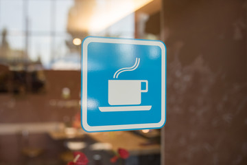 Close up to sticker of symbol coffee shop on glass background. Cafe wallpaper view. sticker on the window with a picture of a cup of coffee. coffee bar sticker on a glass blue
