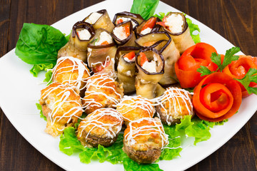 fishballs and meatballs with eggplant rolls with cottage cheese and tomato, parsley on a white plate on a black background