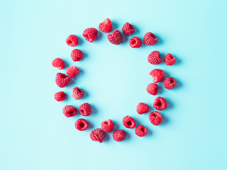 Fototapeta premium Creative layout with fresh ripe berries. Raspberry on blue background with round empty circle in center for copy space. Can use for your design. Top view or flat lay. Negative space for text