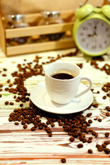 A cup of coffee on a platter with lots of sprinkled coffee beans. Alarm clock arrows at 9 am. Wooden textured table. Shy pastel background. Time to wake up in the morning. Natural food concept