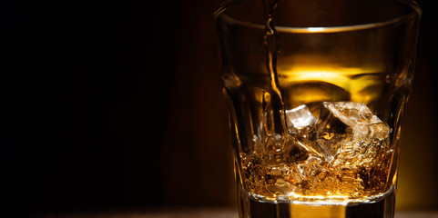 whiskey is poured into a glass with ice on a dark wooden background