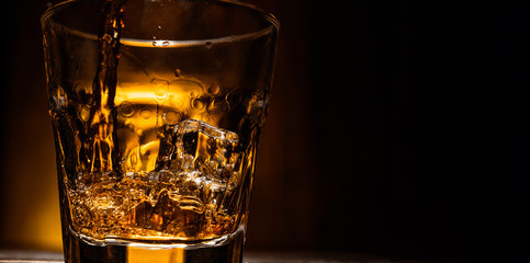 whiskey is poured into a glass with ice on a dark wooden background