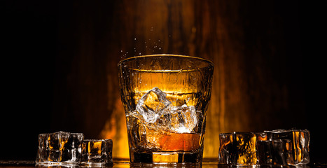ice falls into a glass with expensive whiskey and spray flies in different directions
