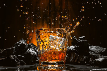 ice falls into a glass with expensive whiskey and spray flies in different directions