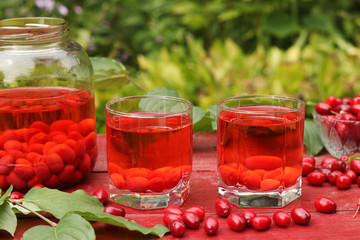 Dogwood compote in two glasses and jar on a wooden table on the garden, Horizontal format, Closeup