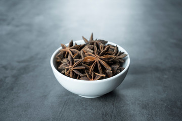 Anise stars in white porcelain bowl on stone, concrete background. 