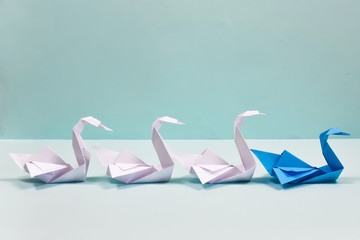 Origami. Paper swans on a blue background. Leadership concept. A blue swan leads a flock of white...