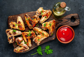 Grilled chicken wings in barbecue sauce on a wooden board on a concrete table.