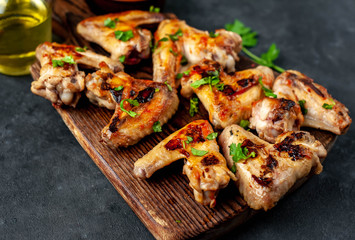 Grilled chicken wings in barbecue sauce on a wooden board on a concrete table.