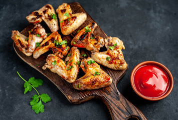 Grilled chicken wings in barbecue sauce on a wooden board on a concrete table with copy space for your text.
