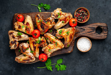 Grilled chicken wings in barbecue sauce on a wooden board on a concrete table.