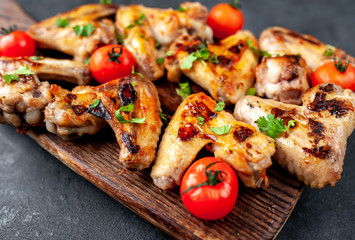 Grilled chicken wings in barbecue sauce on a wooden board on a concrete table.