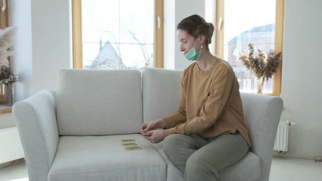 young woman in medical protective mask holding cards and playing solitaire on sofa. Activity, hobby during quarantine of coronavirus pandemic COVID-19, 2019-nCoV. self isolation, stay home concept