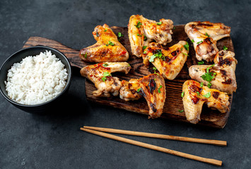 Grilled chicken wings in barbecue sauce and rice in a bowl on a concrete background