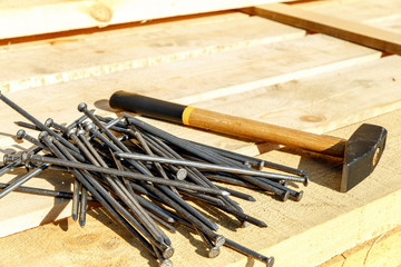 Iron nails and a hammer on a wooden background. Long, metal, carpenter's nails and a mallet lie on a bar for construction. Fixing tool. Side view. space for text.