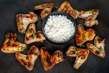 Grilled chicken wings in barbecue sauce and rice in a bowl on a concrete background
