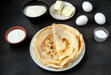 The recipe for making thin home-made pancakes. Ready-made thin pancakes, flour, eggs, butter, milk, sugar on a stone background