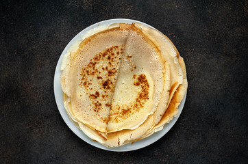 The recipe for making thin home-made pancakes. Ready-made thin pancakes, flour, eggs, butter, milk, sugar on a stone background