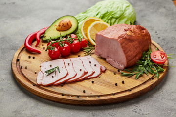 Sliced ham with spices, lettuce, avocado and tomatoes on wooden cutting board. Сold meat plate. Fresh prosciutto
