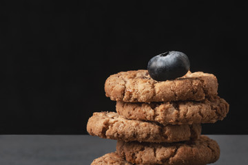 Closeup photo of stack of homemade oatmeal cookies and blueberry on top.