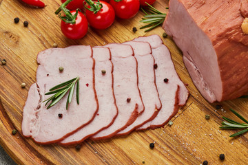 Sliced ham with spices, lettuce, avocado and tomatoes on wooden cutting board. Сold meat plate. Fresh prosciutto
