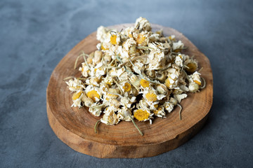 Dried chamomile tea in wooden serving board on stone, concrete background.  Dry, organic, healthy and relaxing herbals.
