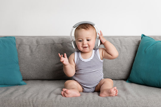 Smiling baby boy sitting on sofa listening to music with headphones