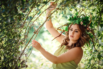Beautiful young woman in a green dress and a wreath in a sunny forest