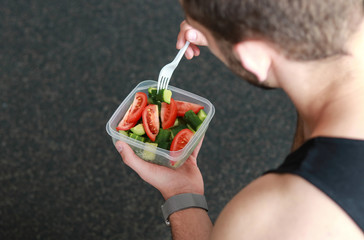 young man sits in a sportswear after training and eats vegetable salad. view from above