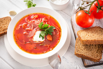plate of Ukrainian red borscht with sour cream and herbs,  spoon, bread, tomatoes, closeup