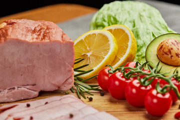 Sliced ham with spices, lettuce, avocado and tomatoes on wooden cutting board. Сold meat plate. Fresh prosciutto