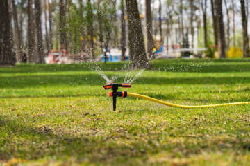 Obraz na płótnie Canvas The portable sprinkler sprinkles abundantly water in the summer heat on the lawn on a bright sunny day.
