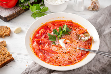 Ukrainian red borscht with parsley and sour cream,  spoon, pieces of bread on a white wooden background, closeup