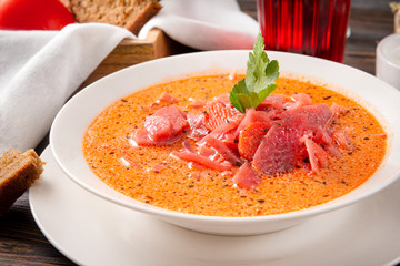 white plate of russian  red borscht with parsley and sour cream ,  spoon, pieces of bread , glass of juice