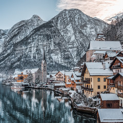 Fototapeta premium Snowy village Hallstatt by lake at foot of snow mountain with clear sky in winter in Austria