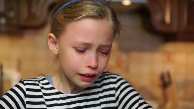 Blond child girl crying heavily tears drop down her face offended in home kitchen. Child abuse bad childhood