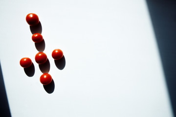 Religious tomatoes. Red cherry Tomatoes lie in the shape of a cross. A dark shadow falls from each tomato. the cross lies in the start of the light.