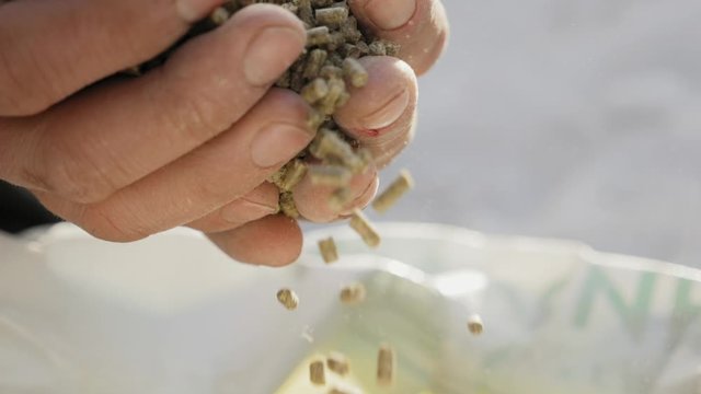Closeup of granulated feed in the hands of a farmer falling to the bag in slow-motion