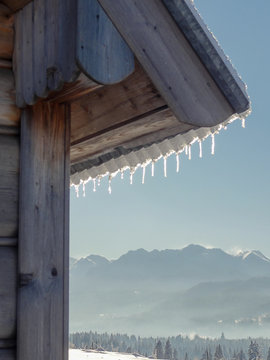 Widok na góry Tatry po stronie polskiej w słoneczny mroźny dzień  z za rogu drewnianego domu z soplami lodu na dachu