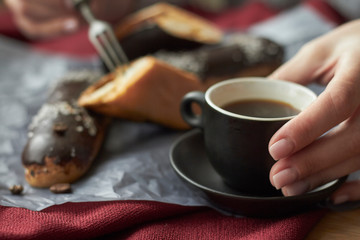 Woman eating eclairs filled with cream, traditional french eclairs with chocolate and cup of espresso, selective focus.