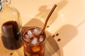 Cold brew coffee with ice cubes in glass on wooden tray,beige background,hard light,top view