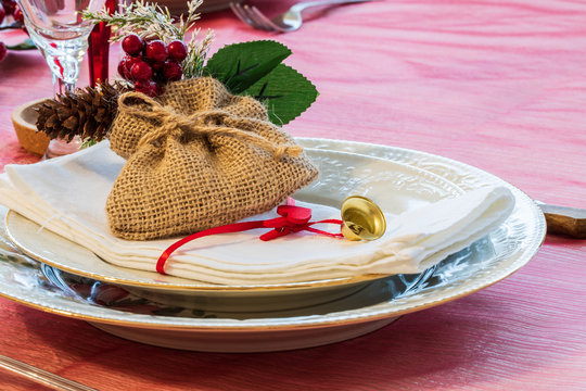 Preparations for the end of year dinner at home. A set table with a small bag, a heart-shaped clothespin and a yellow bell used as decorations on two porcelain plates.