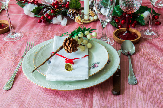 Preparations for the end of year dinner at home. A set table with porcelain dishes, cutlery and various Christmas decorations like a pine cone and a small golden bell.