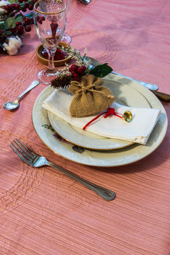 Preparations for the end of year dinner at home. A set table with porcelain dishes, cutlery and various Christmas decorations like a small bag and a little golden bell.