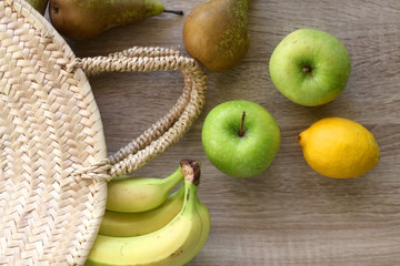 Apples, pears, bananas and lemon in a straw bag. Top view.
