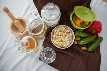 Decorated with lettuce, side view, selective focus . Orange pepper in a green bowl . Water in a glass. Brown tablecloth. Salad with ham, bell pepper, mushrooms, pickles, white sauce, on a white plate.