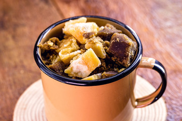 enamelled rustic mug with sweets inside, pieces of brown sugar, typical Brazilian food for June and July parties, rural and country tradition of Brazil.